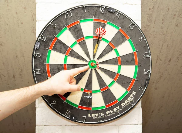 a man shows a dart stuck in the center of the darts, the result of skill and victory.