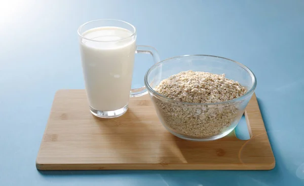 一杯牛奶和一个装有燕麦片的玻璃碗放在木板上 蓝色背景 健康简单的早餐 — 图库照片