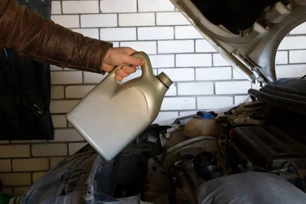 a man begins to pour motor oil from a plastic canister with synthetic motor oil. concept of repair and oil change on a car