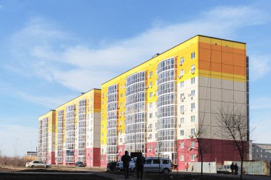 Mavi gökyüzünün arka planında çok katlı yeni bir binanın görüntüsü. Binanın duvarları turuncu, kırmızı ve beyaza boyanmış.