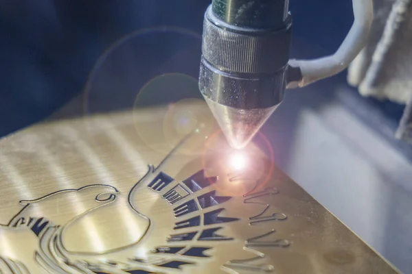 A laser engraving machine cuts out a picture on a gold glossy plastic plate. Closeup