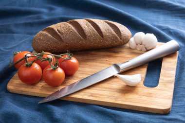 Taze ekmek, domates, sarımsak, kesme tahtasındaki bıçak. Koyu mavi arka plan. Yan görüş. Yakın çekim.