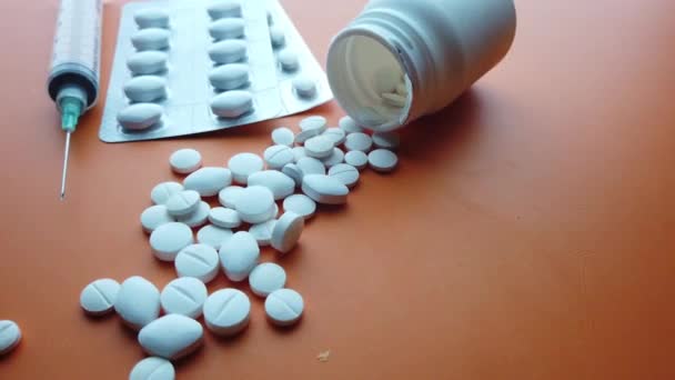 Разлив таблеток и шприц на цветном фоне — стоковое видео
