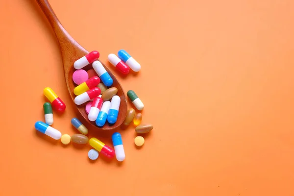 Färgglada piller och kapsel på sked på orange bakgrund — Stockfoto