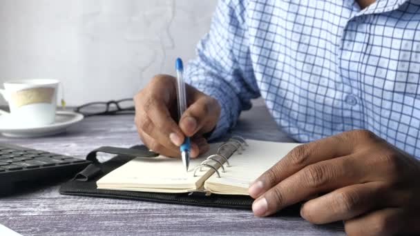 Közelkép egy üzletemberről, aki jegyzetfüzetre ír. — Stock videók