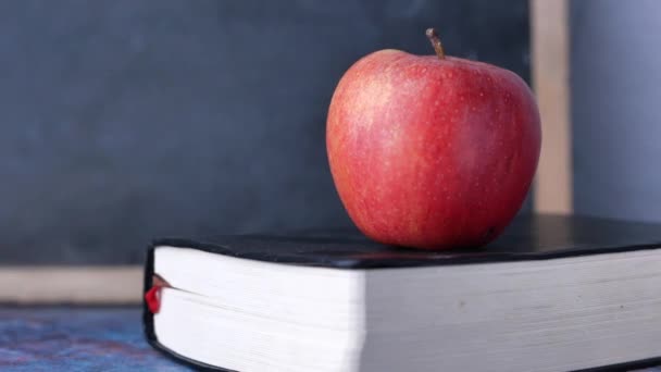 Κοντινό πλάνο του μήλου σε ένα βιβλίο ενάντια σε έναν πίνακα — Αρχείο Βίντεο