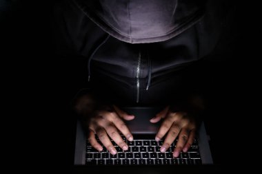 top view of hooded hacker sealing data from laptop 