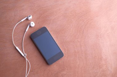 Masadaki akıllı telefon ve kulaklığın üst görüntüsü 