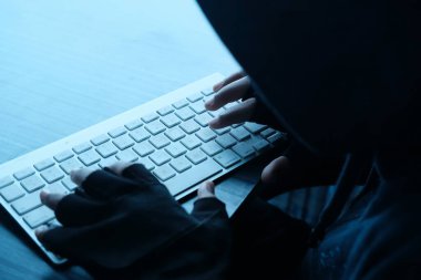 top view of hooded hacker sealing data from laptop 