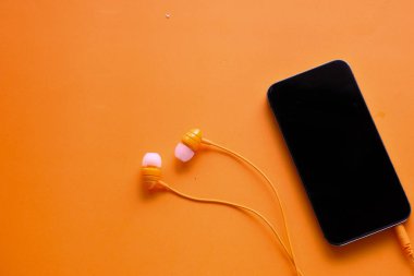 Turuncu arka planda akıllı telefon ve kulaklığın üst görüntüsü 