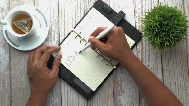 Vista superior de la mano del hombre escribiendo objetivos de año nuevo en el bloc de notas — Vídeo de stock