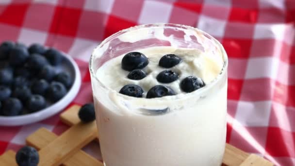 Großaufnahme von blauen Beeren auf Joghurt auf dem Tisch — Stockvideo