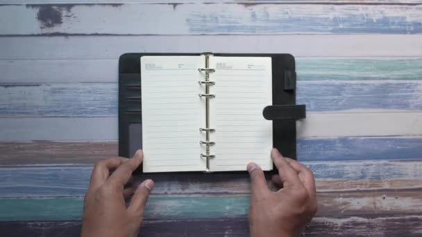 Человек, переворачивающий страницы дневника на столе — стоковое видео
