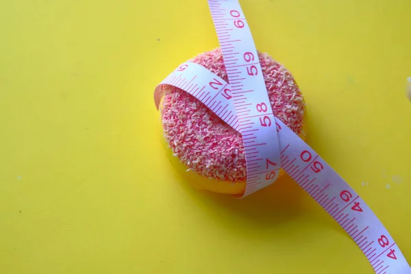 Measuring tape and colorful donuts on yellow background, close up — Stockfoto