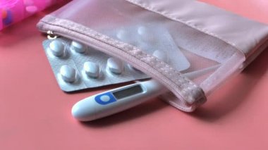  white pills ,thermometer and pill box on pink background 