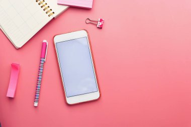 Pembe arkaplanda akıllı telefon, not defteri ve klavyenin üst görünümü 
