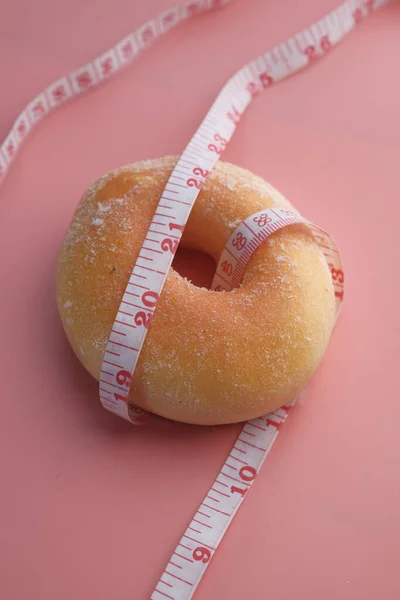 close up of measurement tape and donuts on pink background