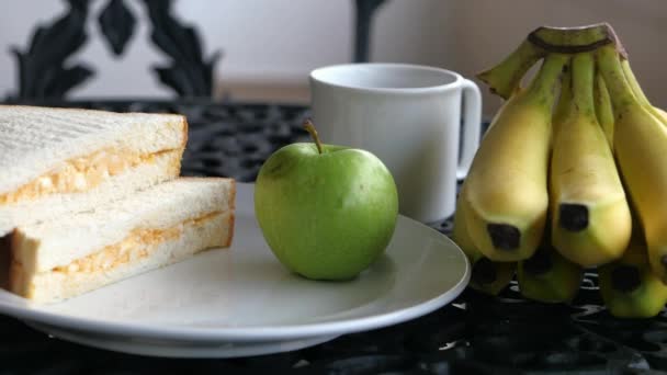 Утренний завтрак с бананом, хлебом, чаем и яблоком на столе — стоковое видео