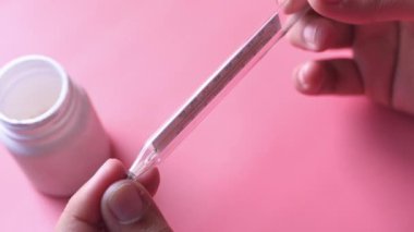 Kırpılmış kadın pembe üzerinde plastik kap ve termometre taşıyor.