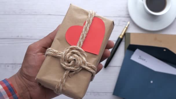 Чоловік тримає подарунок у формі серця та конверт на столі — стокове відео