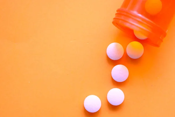 Λευκά χάπια χυμένα σε πορτοκαλί φόντο, κοντά . — Φωτογραφία Αρχείου
