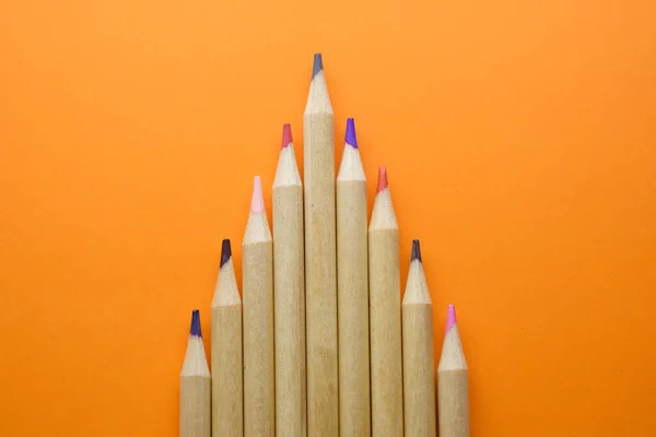 Lápis multicoloridos linha crescente isolado em laranja — Fotografia de Stock