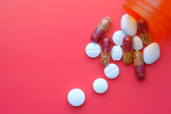 Colorful pills pilling from container on red background — Stock Photo, Image