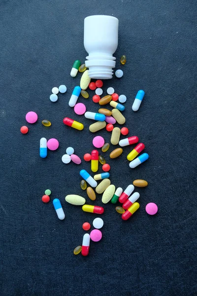 Kleurrijke pillen morsen uit container op zwarte achtergrond, bovenaanzicht — Stockfoto