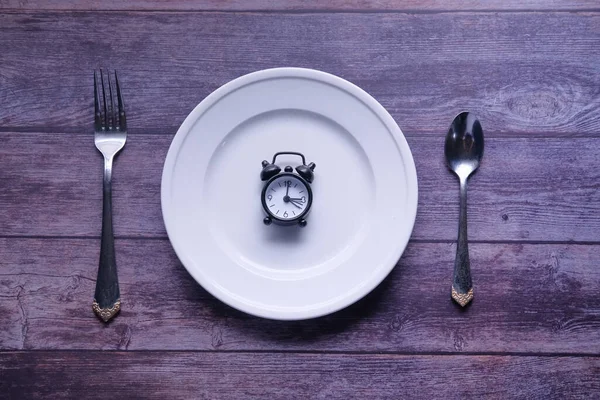 Alarm clock with fork, knife and plate on the table. Top view. Time to eat