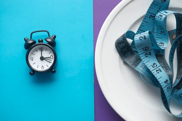 Um relógio sobre fundo de cor e fita métrica, conceito de dieta de jejum intermitente — Fotografia de Stock