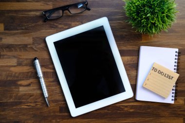 Tahta masadaki dijital tablet, kalem ve not defterinin üst görünümü 