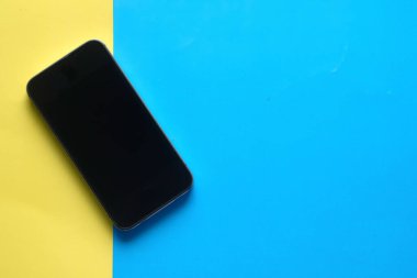 Çapraz pastel sarı ve mavi arkaplanda boş ekran cep telefonu.