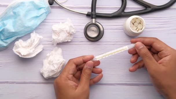 Hombre mano celebración termómetro con pastillas y estetoscopio en la mesa — Vídeos de Stock