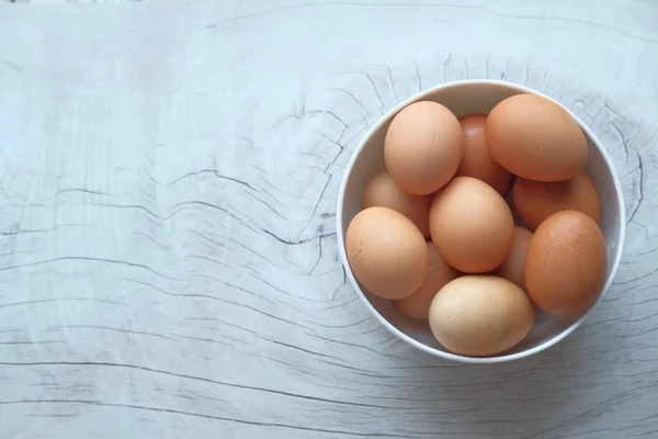 Oeufs dans un bol en bois sur une vieille table en bois vue sur le dessus. — Photo