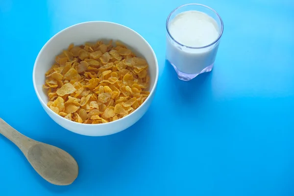 Sabrosos copos de maíz crujientes con leche sobre fondo azul . — Foto de Stock