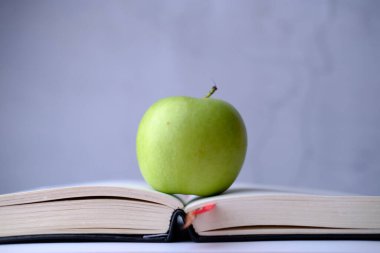 Yeşil elmayı beyaz üzerine izole edilmiş kitaba yaklaştır .