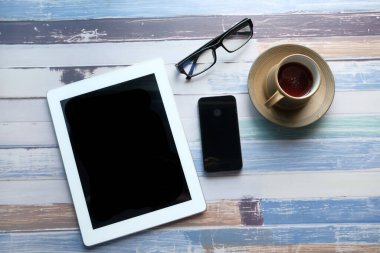 Dijital tabletin üst görüntüsü, akıllı telefon, ahşap masadaki kalem ve çay. 