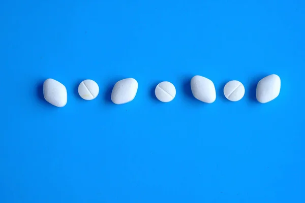 Weiße Pillen in einer Reihe auf blauem Hintergrund — Stockfoto