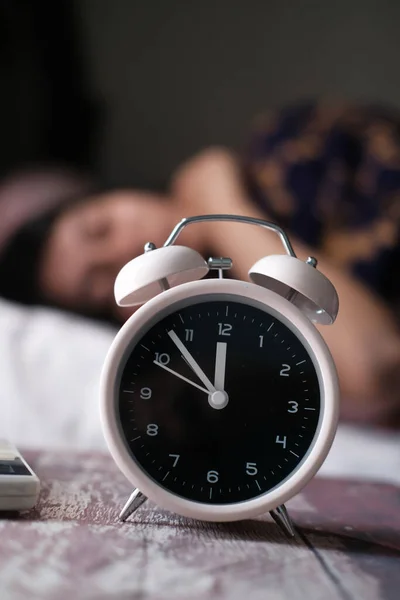 Reloj despertador en mesa con mujer durmiendo sobre fondo —  Fotos de Stock