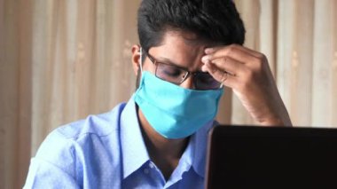 Yüzünde antivirüs koruması maskesi olan hasta bir adam dizüstü bilgisayarla çalışıyor. 