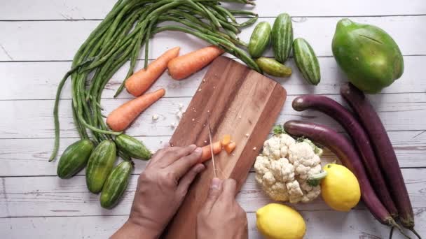 Руки людини, що ріже моркву на рубаній дошці на кухні . — стокове відео