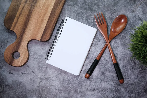 Bloco de notas na tábua de cortar com garfo de madeira e colher na mesa branca . — Fotografia de Stock