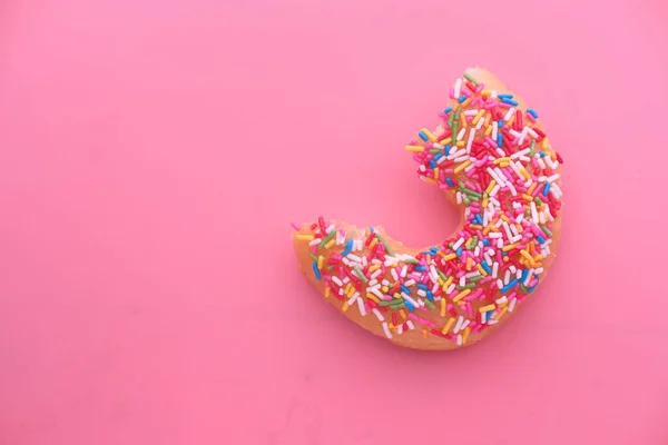 Donut medio comido sobre fondo rosa — Foto de Stock