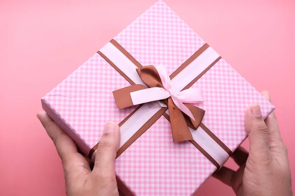 Mano de las mujeres sosteniendo caja de regalo de color rosa sobre fondo rosa . — Foto de Stock