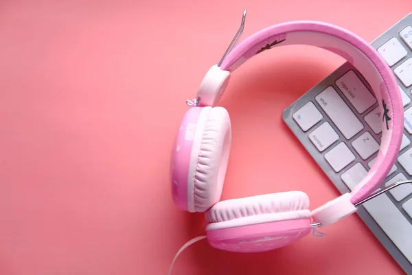 headphones and keyboard on pink background, close up