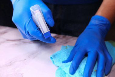 Elinde sprey şişesi tutan mavi lastik eldivenler. 