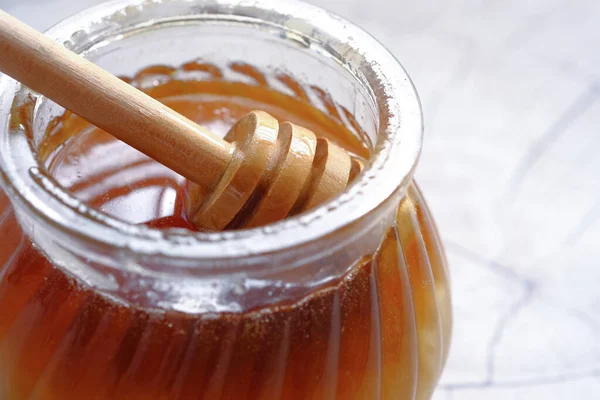 Cucchiaio in un vaso di vetro di miele su sfondo bianco . — Foto Stock
