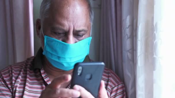 Ανώτερος άνθρωπος με μάσκα χρησιμοποιώντας έξυπνο τηλέφωνο εσωτερικού χώρου — Αρχείο Βίντεο