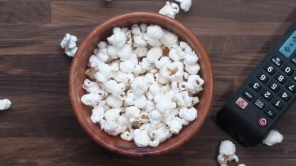 Een kom popcorn, TV afstandsbediening op tafel — Stockvideo