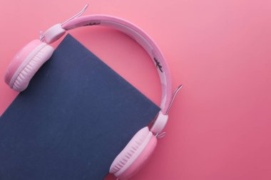 Pembe arka planda kitap ve kulaklık. Kapat.